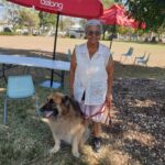 white-haired lady stands near her German Shepherd dog, wearing a red lead