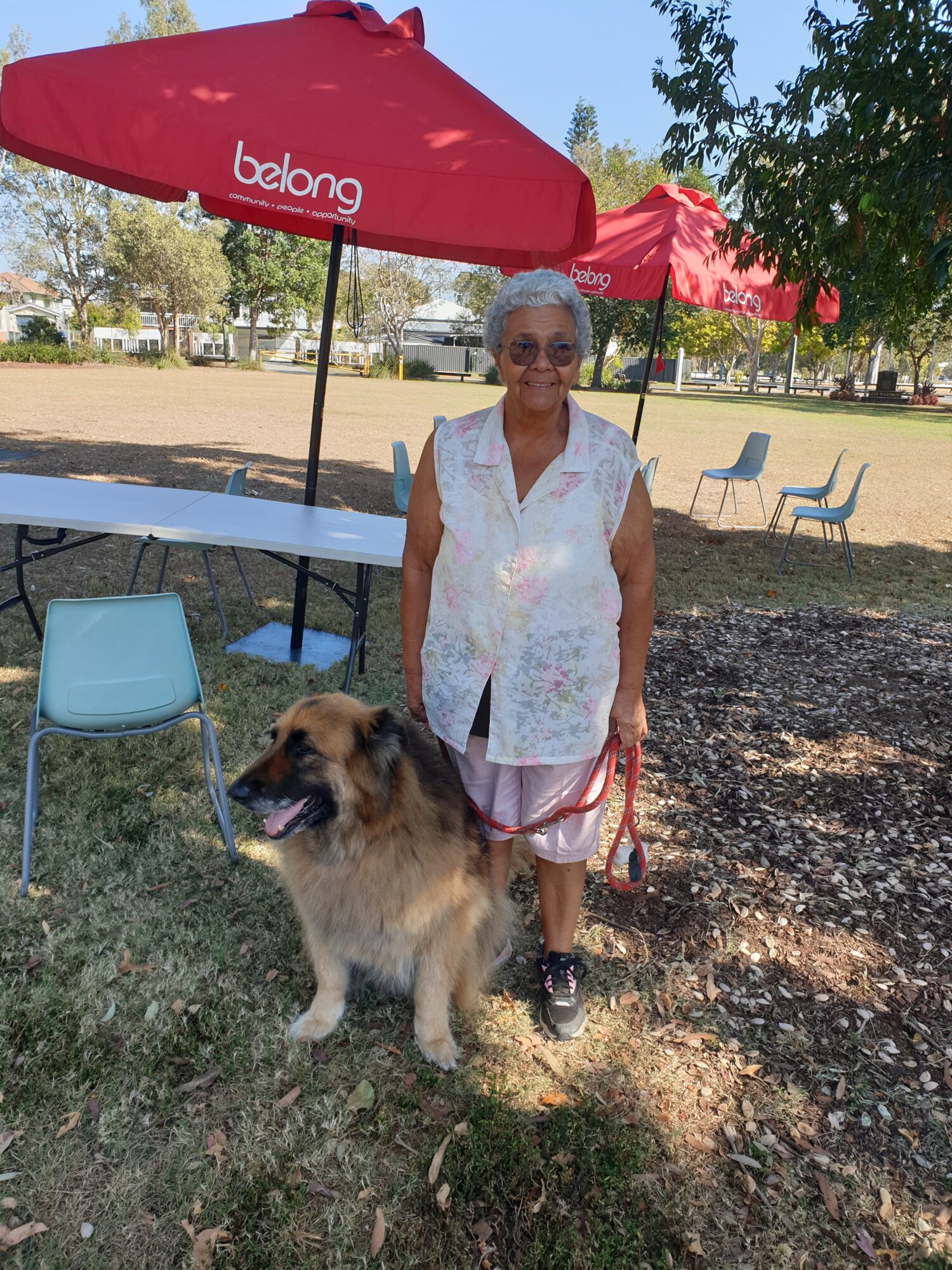 white-haired lady stands near her German Shepherd dog, wearing a red lead