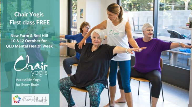 A group exercise session for seniors featuring a female instructor assisting an older woman with short gray hair wearing a black top and patterned leggings. The instructor, wearing a white tank top and blue leggings, demonstrates a stretch. Two other women, one with brown hair in a bun wearing a purple top and the other with light brown hair in a ponytail wearing a blue top, follow along, all appearing focused and engaged.