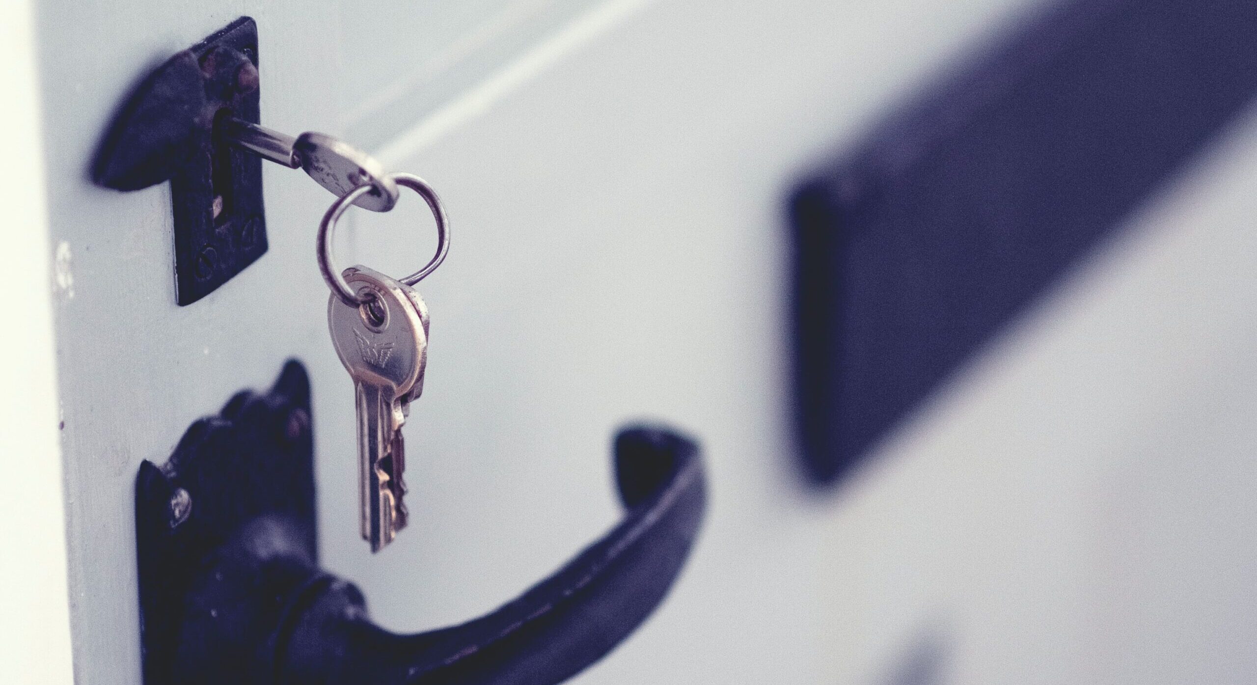 Close-up of a metal key hanging from a hook, symbolizing security and access. The key is silver and reflects light, set against a blurred background.